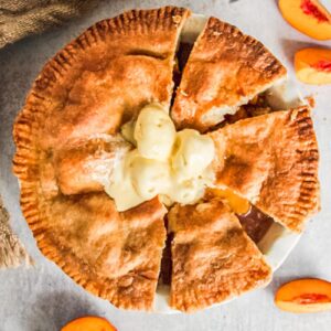 Double crusted peach cobbler sits with slices cut out on a gray surface.