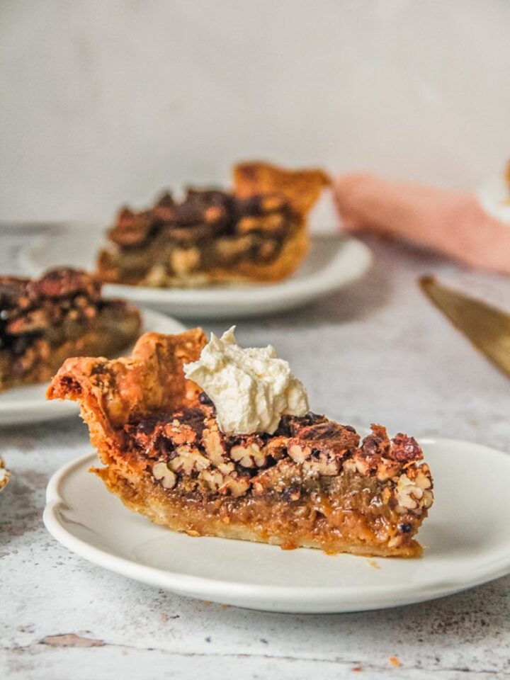 A slice of Pecan Pie sits on a white ceramic plate on a light gray surface.