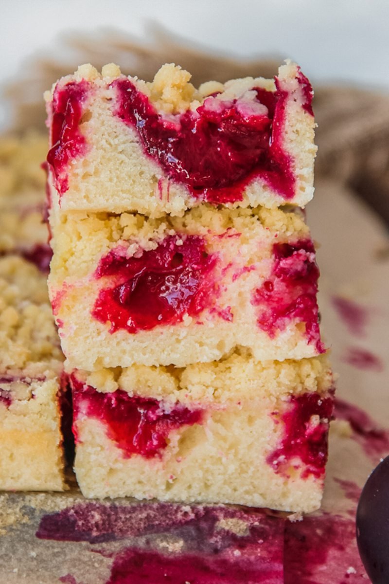 Slices of plum streusel cake sit stacked on each other on parchment paper.