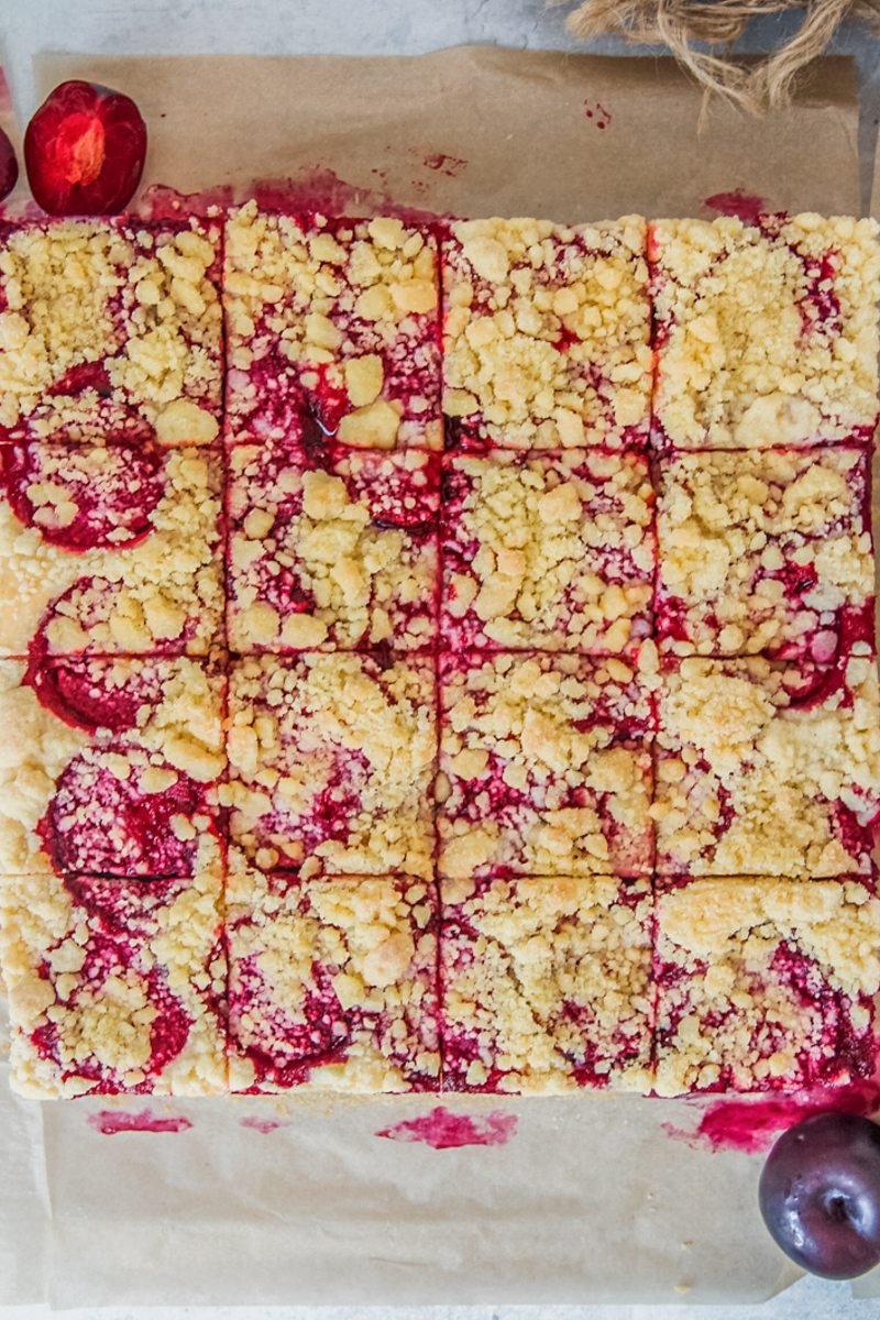 Czech Plum Cake sits on a gray surface on brown parchment paper with 16 slices cut into the plum cake.