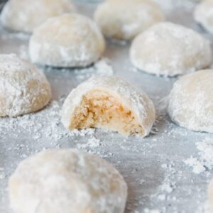 A close up of a halved Polvorone or Mexican Wedding Cookie sitting with other cookies on a gray surface.