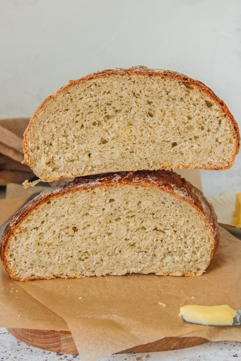 German potato bread sits halved on parchment paper on a wooden board on a gray surface with butter in the background.