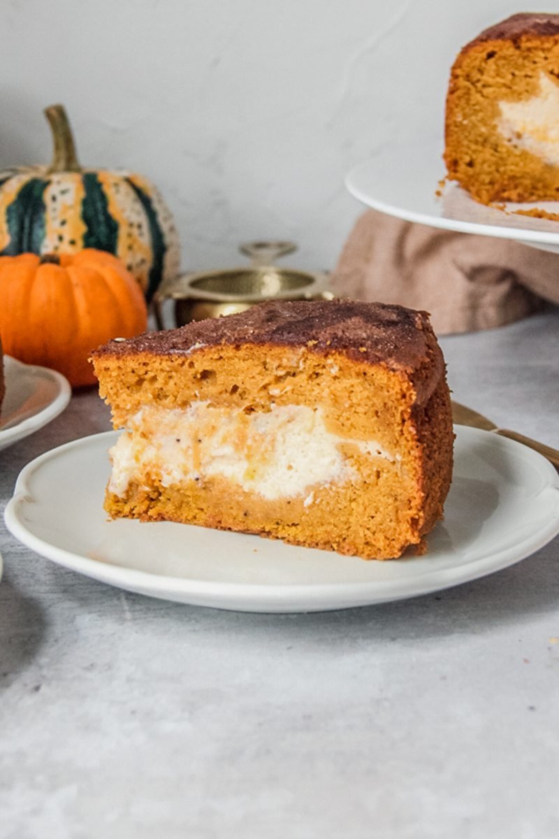 A slice of pumpkin cake is served up on a white plate with the cream cheese center visible.