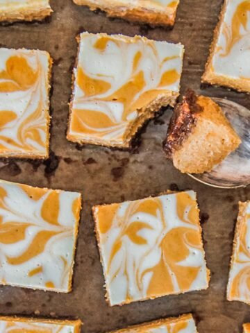 A spoonful of pumpkin cheesecake sits beside pumpkin cheesecake bars on parchment paper.