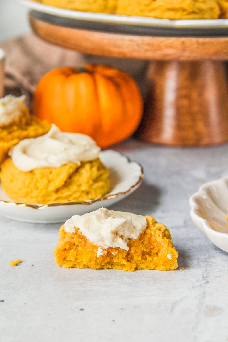 A halved pumpkin sugar cookie sits on a gray surface with a maple buttercream frosting in the center.