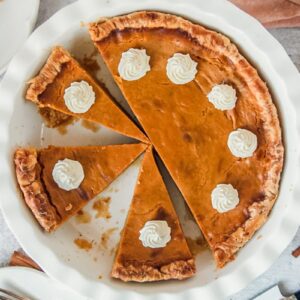 Pumpkin pie with slices cut into it sit in a white ceramic baking dish.