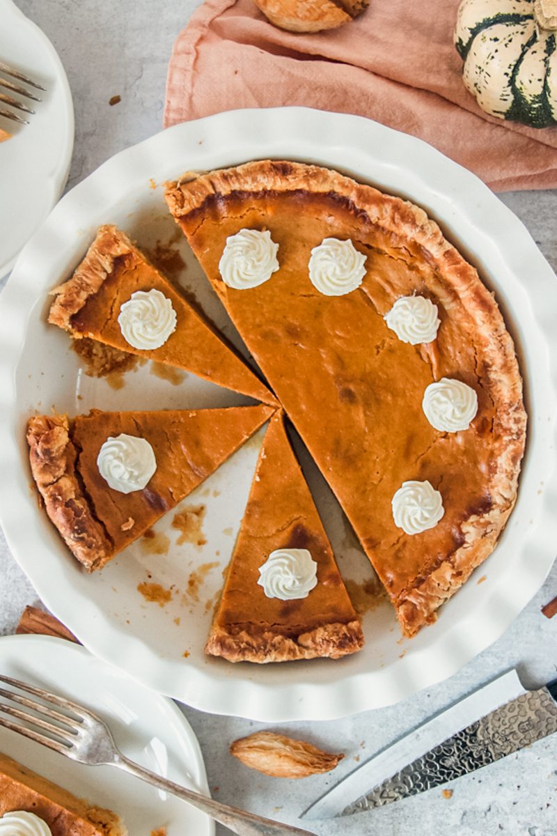 Pumpkin pie with slices cut into it sit in a white ceramic baking dish.