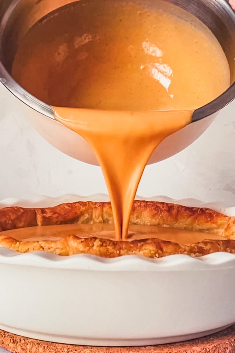 Pumpkin pie filling is poured into a parbaked crust in a white ceramic dish.
