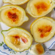 Lemon posset sits on a floral plate with caramelized tops on a light gray surface and a spoonful of the posset resting on the edge of the plate.