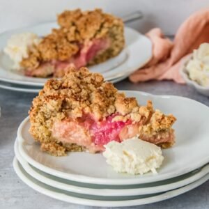 A slice of Icelandic Happy marriage rhubarb cake sits on a stack of white ceramic plates on a gray surface.