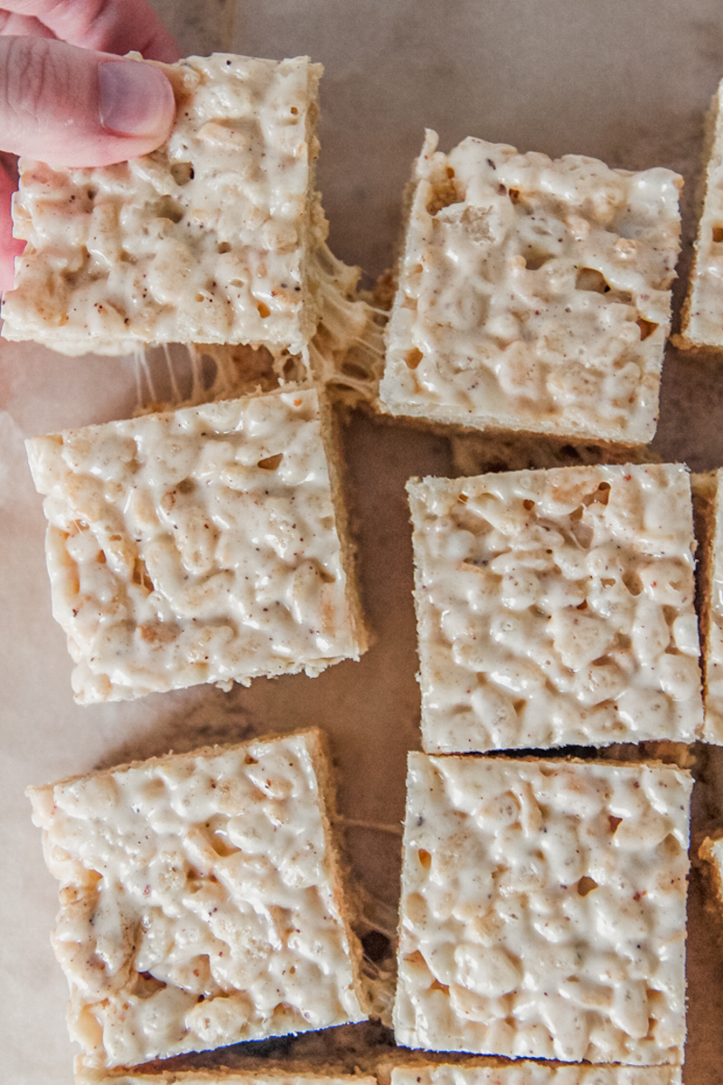 A square of rice krispie treats is pulled from other treats sitting on parchment paper.