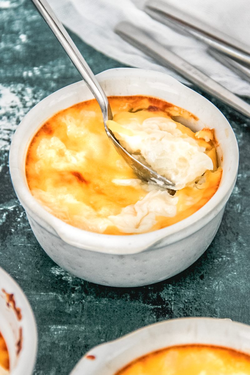 A spooful of rice pudding rests on top of baked golden Turkish rice pudding on a speckled white and green surface.