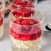 A close up of homemade custard and roasted strawberries sit in glasses on a gray surface.