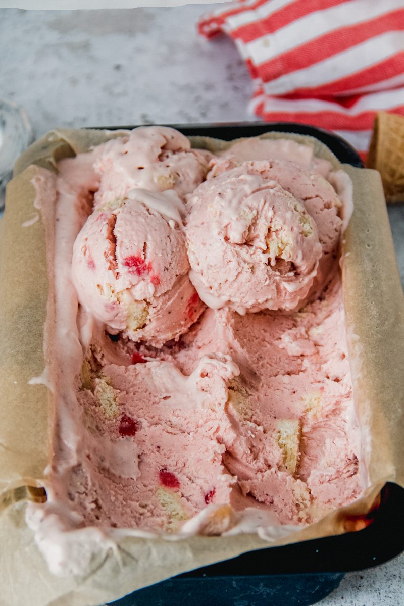 Scoops of Strawberry Shortbread semifreddo sit on top of lined rectangle metal tin on a light gray surface.