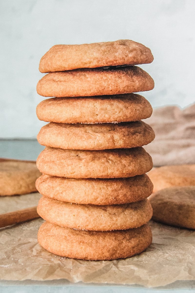 Snickerdoodle cookies sit stacked on each other on parchment paper.