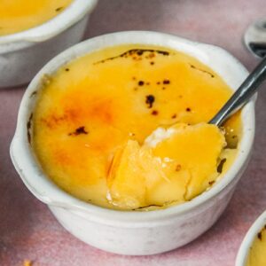 A spoonful of custard is heaped up from a gray ceramic ramekin on a pink surface.