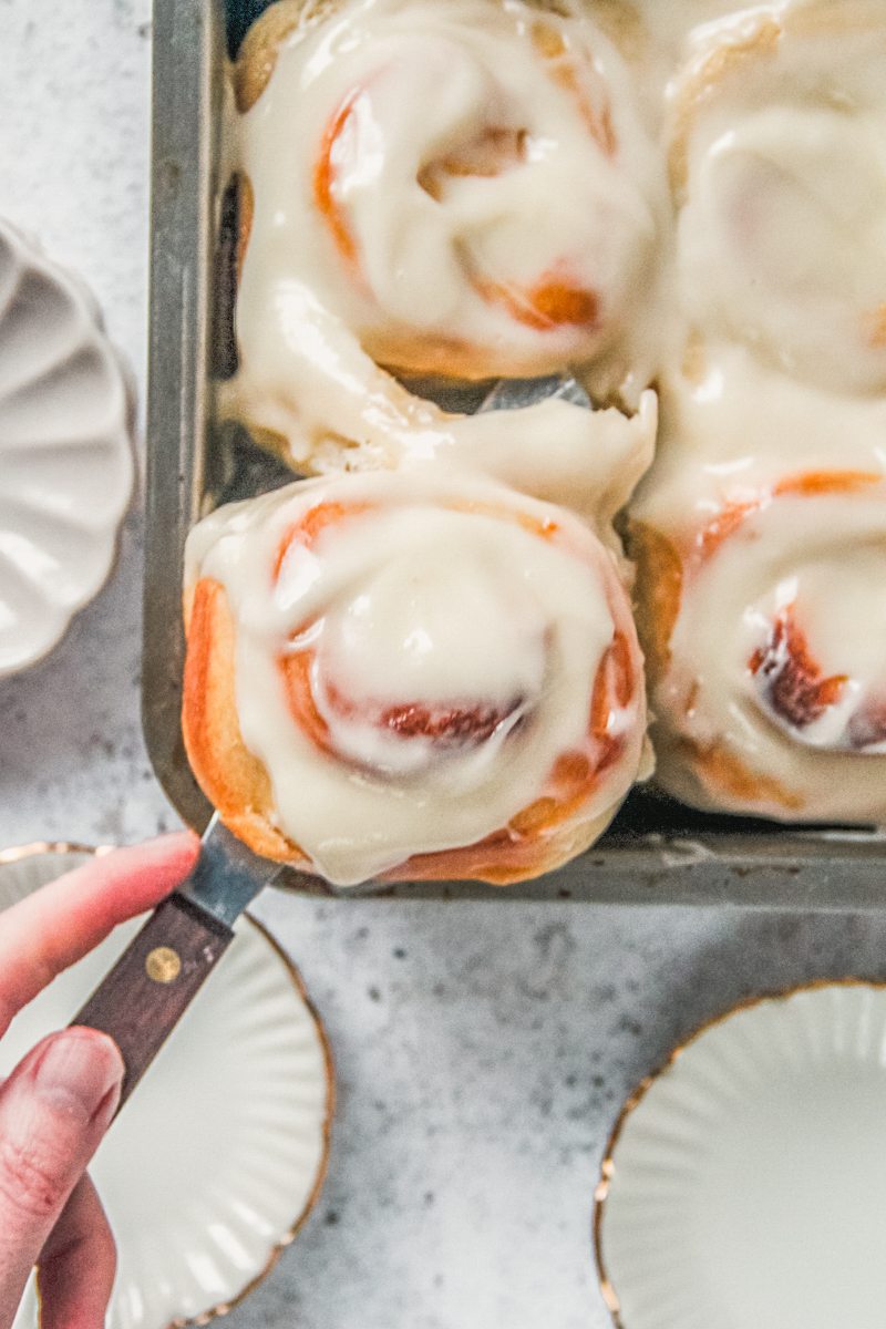 A lemon roll is served up from the baking tin on a light gray surface.