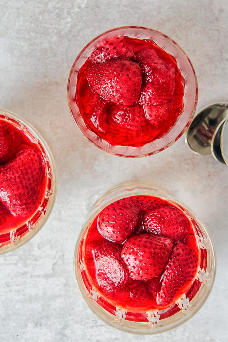 Servings of roasted strawberries and custard sit in glasses on a gray surface.