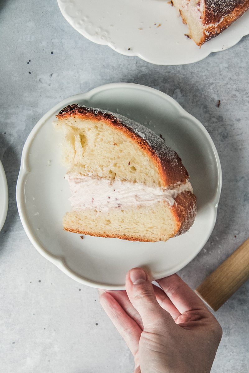 A slice of Sufganiyot or Donut cake lays on an individual white ceramic plate with the jam cream filling visible on a gray surface.