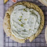 A close up of a pistachio sugar cookie topped with a pistachio buttercream on a lined cooling rack.