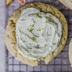 A close up of a pistachio sugar cookie topped with a pistachio buttercream on a lined cooling rack.