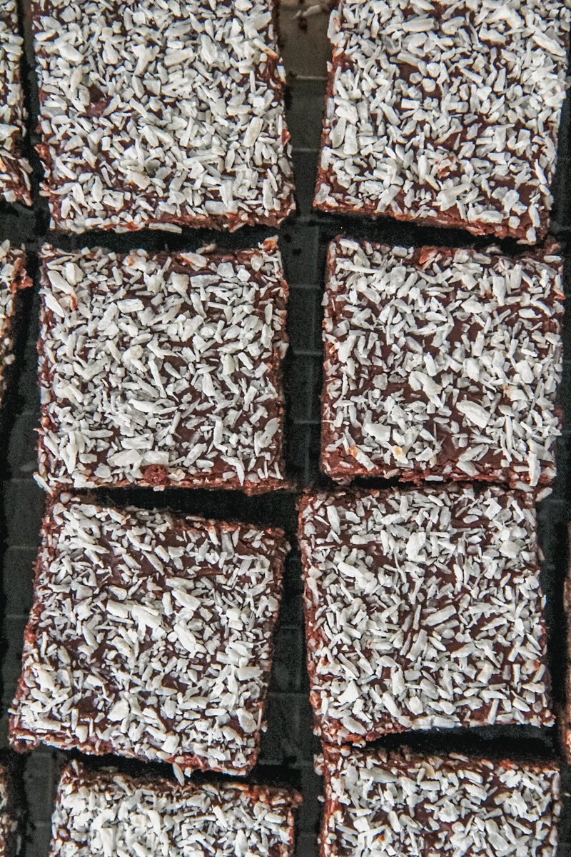 Cubes of Swedish Karleksmums - Love Treats chocolate cake topped with chocolate frosting and desiccated coconut on a cooling rack.