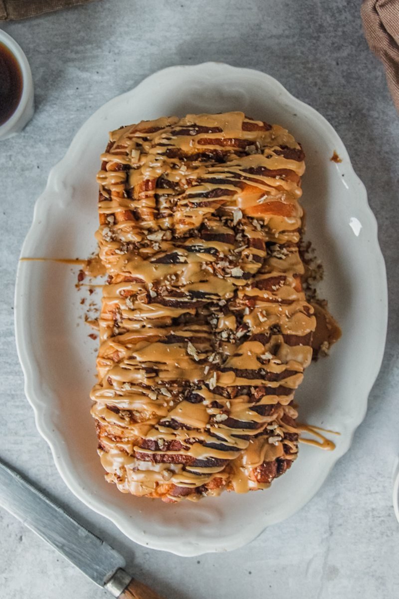 An overhead view of sweet potato babka with coffee glaze served up on a white oval plate on a gray surface.