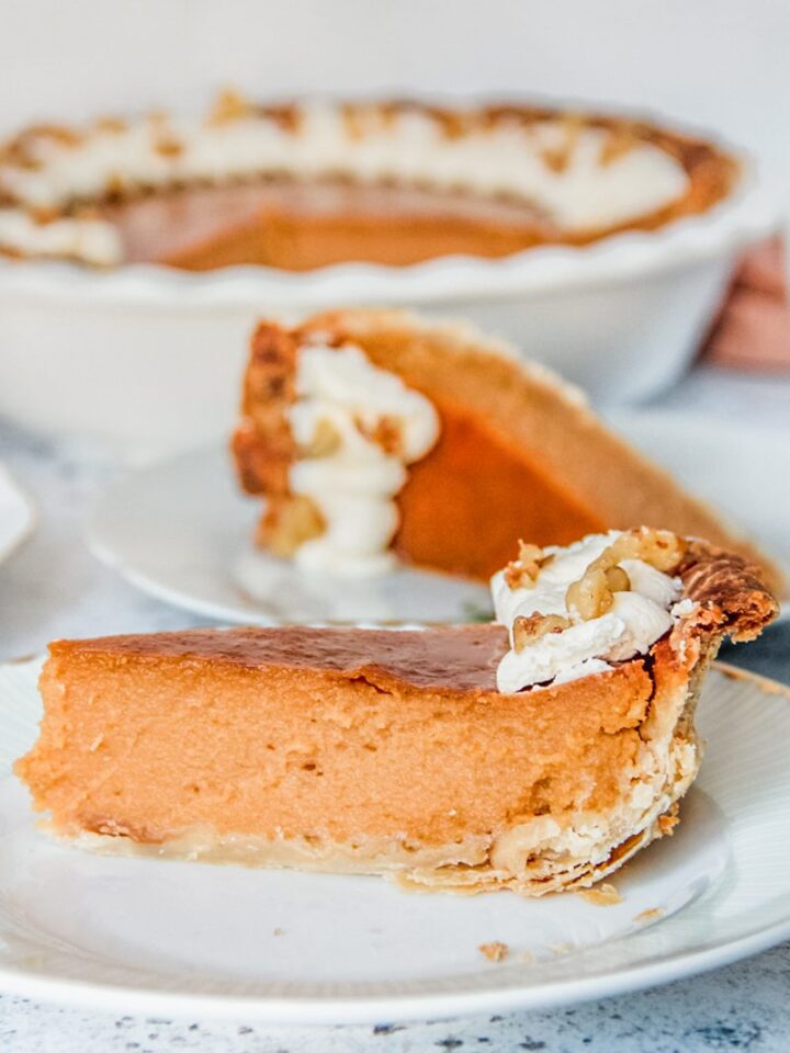 A slice of sweet potato pie has it's close up on an individual plate on a light gray surface.