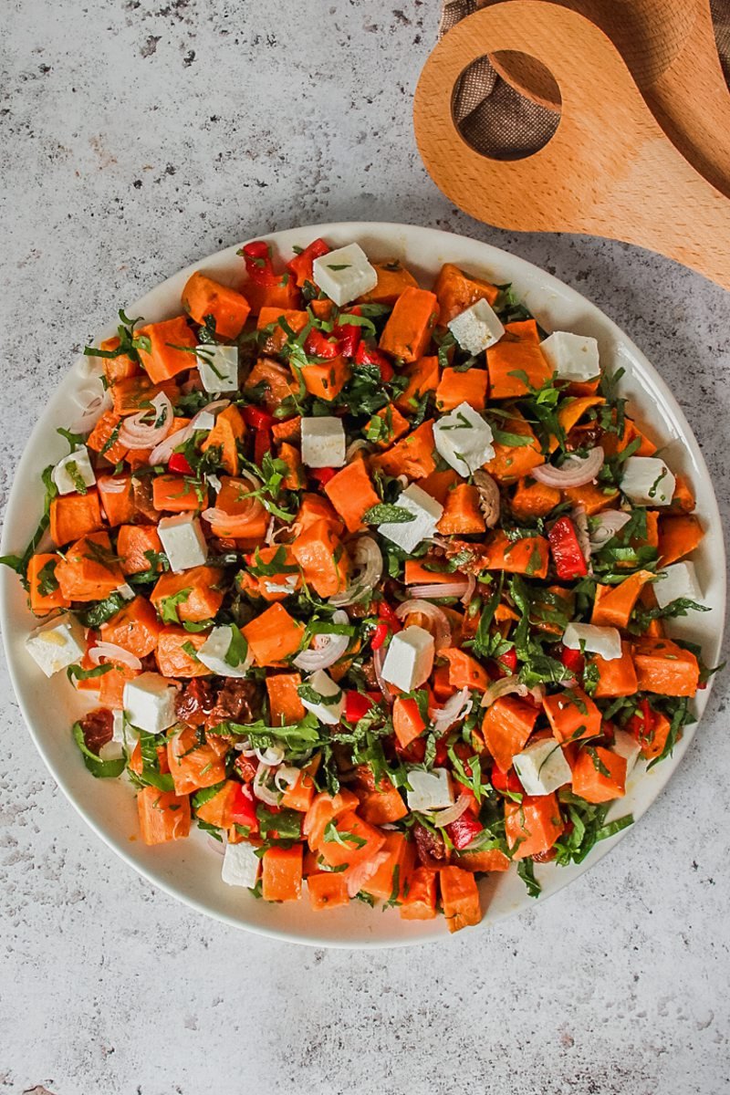 A sweet potato salad sits on a round white ceramic plate on a gray surface.