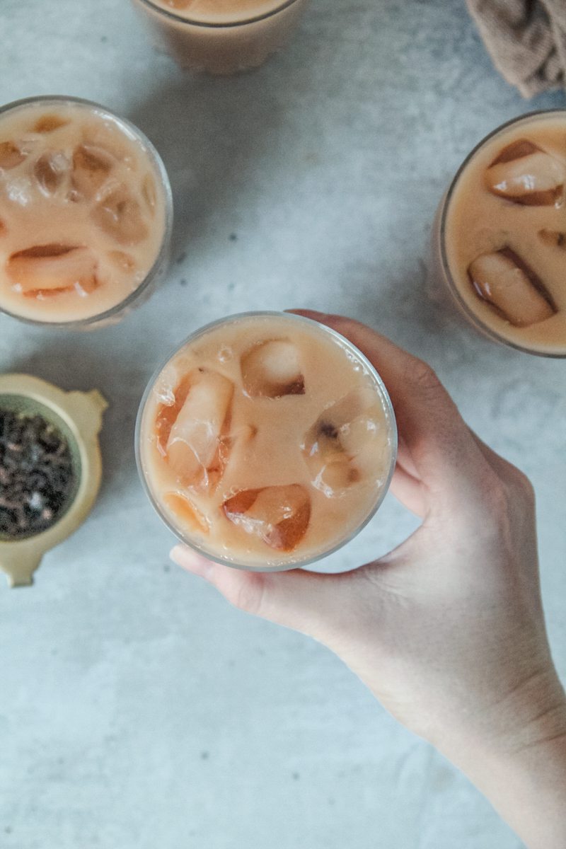 A glass of Thai ice tea is picked up from a gray surface.