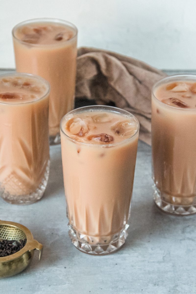 Individual glasses of Thai ice tea sit on a gray surface.