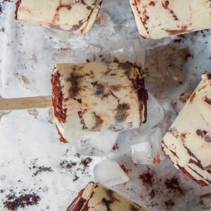 Tiramisu posicles rest on ice cubes on a light gray surface.