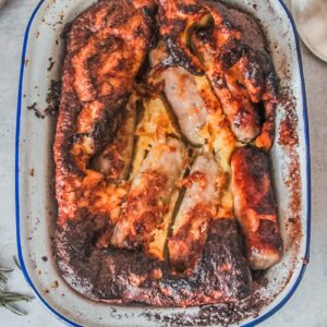 Golden toad in a hole sits in an enamel baking tin on a gray surface.