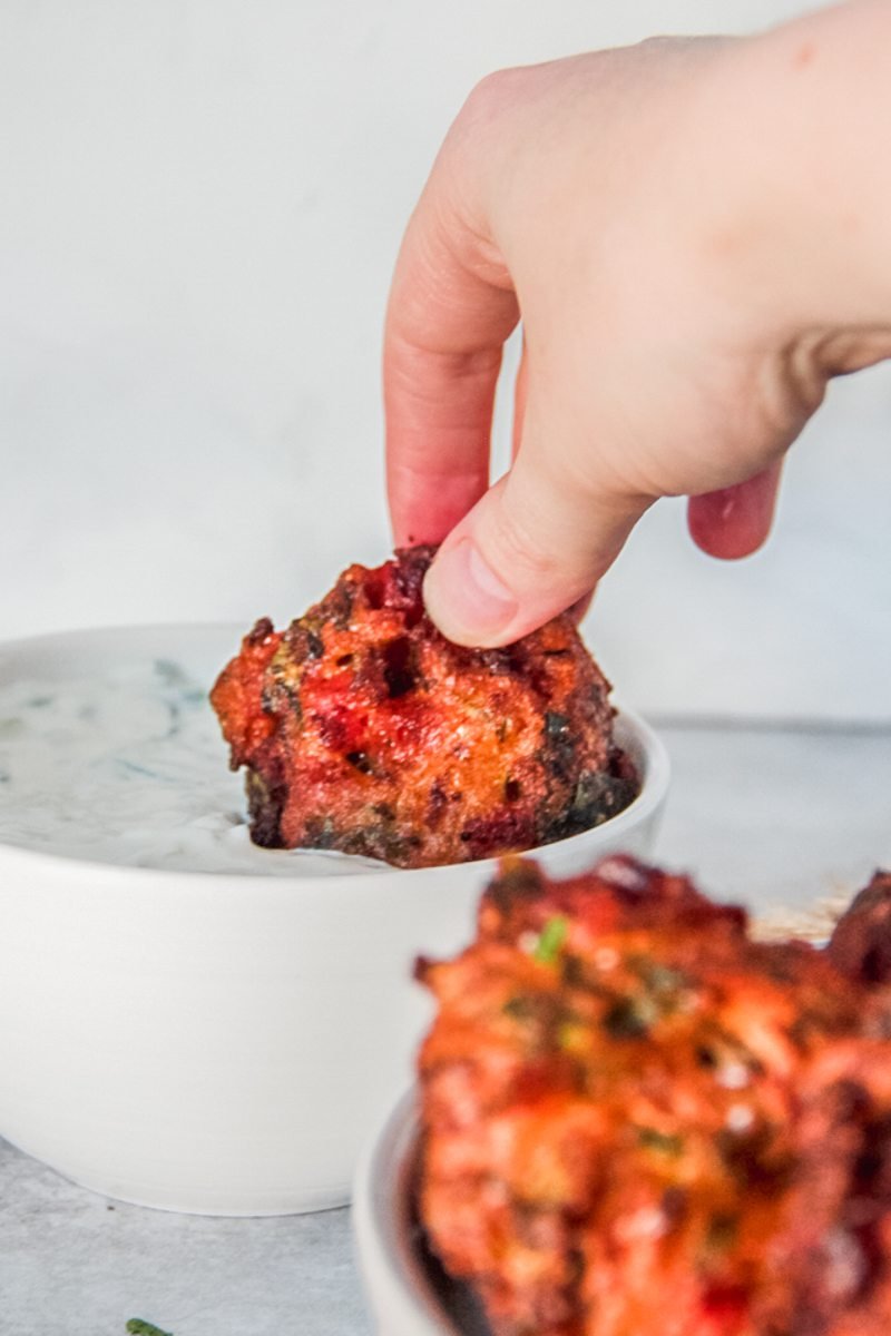 A Greek tomato fritter is dipped into a sauce.