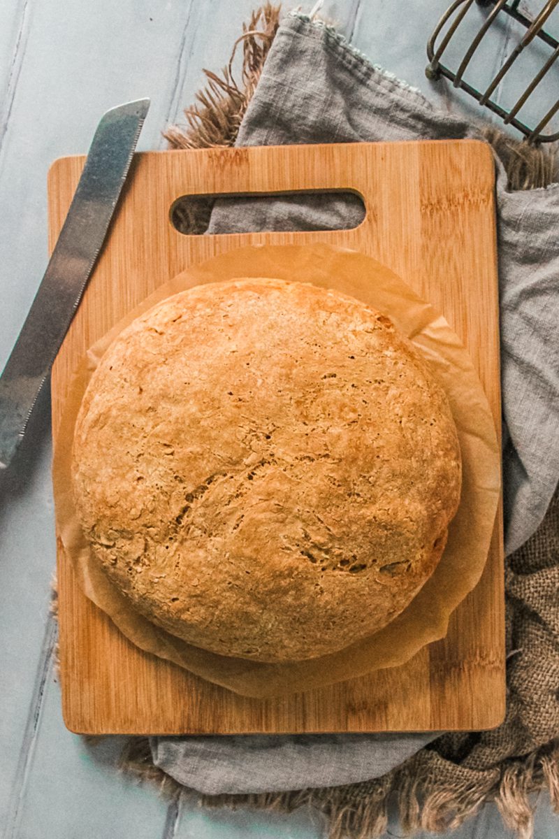 A Native American Masa bread sits on a wooden board on gray and brown clothes on a blue surface.