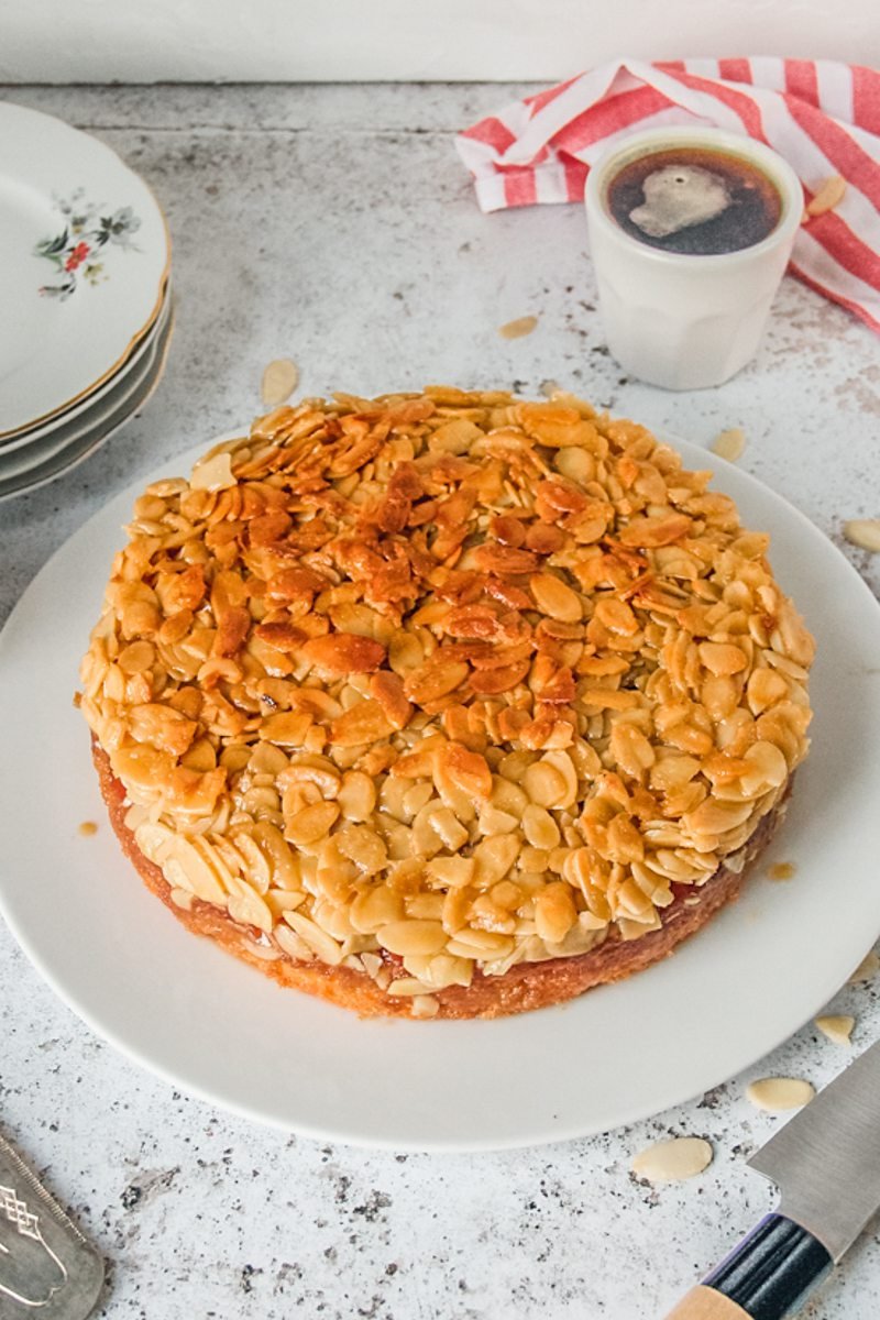 Toscakaka Cake or Swedish Almond Cake sits on a white ceramic plate on a light gray surface.