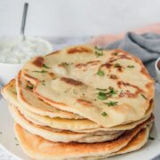 Bazlama - Turkish flatbread sits stacked on a white plate on a gray surface.