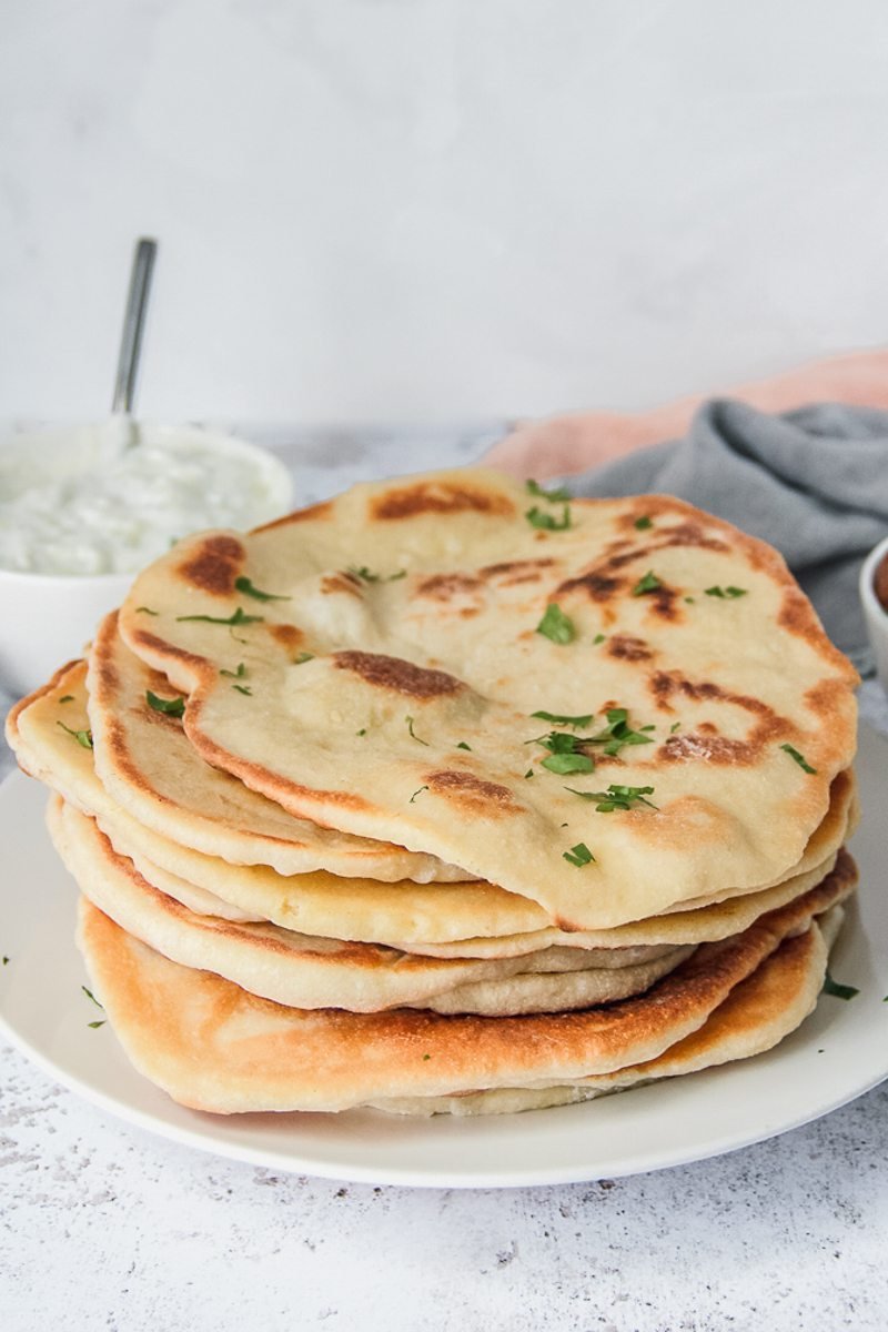 Bazlama - Turkish flatbread sits stacked on a white plate on a gray surface.