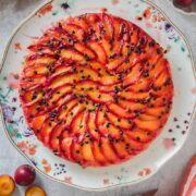 An upside down plum passionfruit cake sits on a floral serving plate on a gray surface.