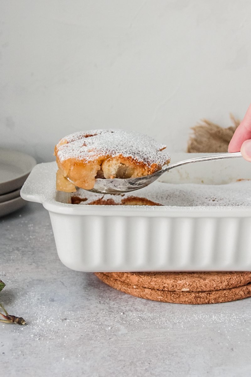 Welsh apple pudding is served up with a serving spoon on gray surface.