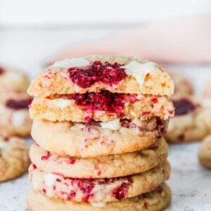 A stack of white chocolate raspberry cookies sit on top of each other on a light grey surface.